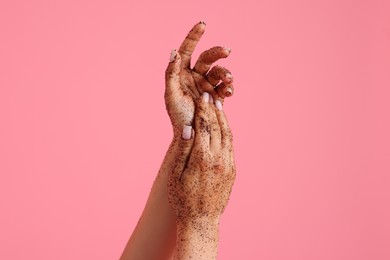 Photo of Woman applying body scrub onto her hands on pink background, closeup