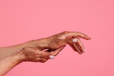 Photo of Woman applying body scrub onto her hands on pink background, closeup