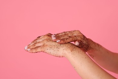 Photo of Woman applying body scrub onto her hands on pink background, closeup