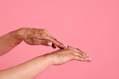 Photo of Woman applying body scrub onto her hands on pink background, closeup
