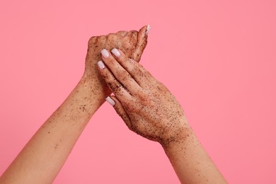 Photo of Woman applying body scrub onto her hands on pink background, closeup