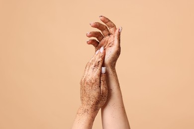 Photo of Woman applying body scrub onto her hands on beige background, closeup