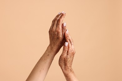 Photo of Woman applying body scrub onto her hands on beige background, closeup