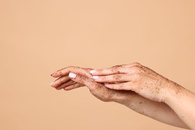 Photo of Woman applying body scrub onto her hands on beige background, closeup