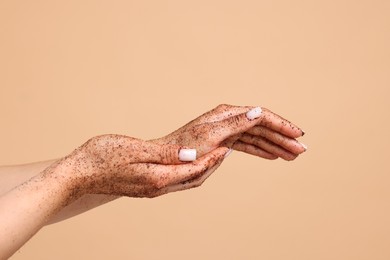 Photo of Woman applying body scrub onto her hands on beige background, closeup