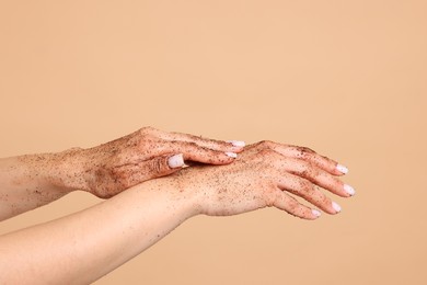 Photo of Woman applying body scrub onto her hands on beige background, closeup