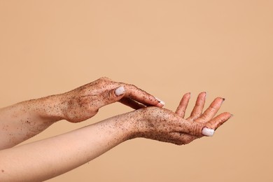 Photo of Woman applying body scrub onto her hands on beige background, closeup
