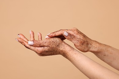 Photo of Woman applying body scrub onto her hands on beige background, closeup