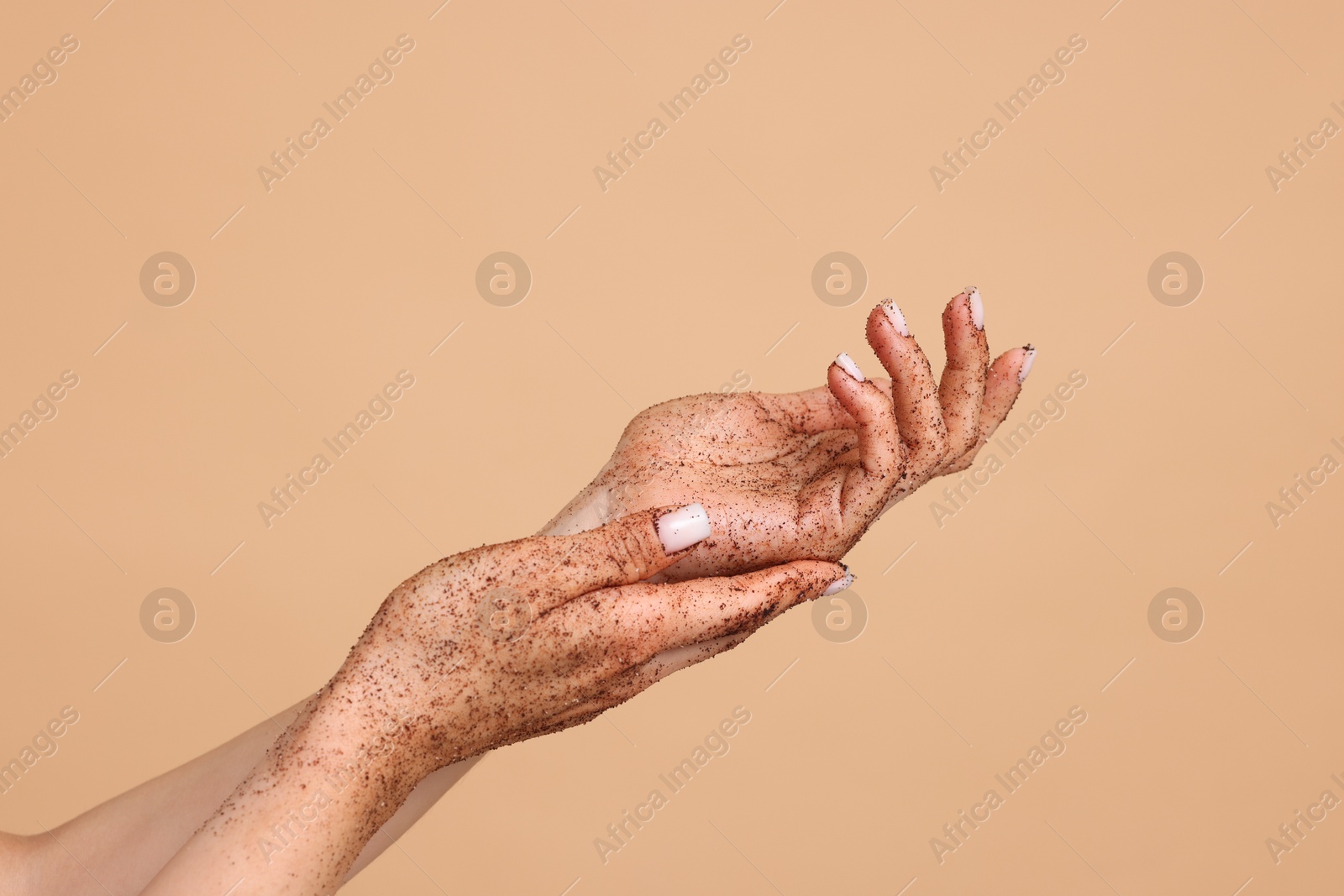 Woman applying body scrub onto her hands on beige background, closeup Photo of Woman applying body scrub onto her hands on beige background, closeup