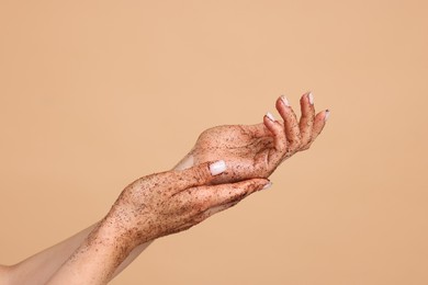 Photo of Woman applying body scrub onto her hands on beige background, closeup