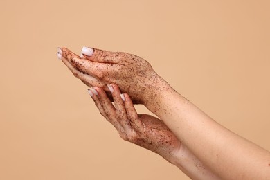 Photo of Woman applying body scrub onto her hands on beige background, closeup