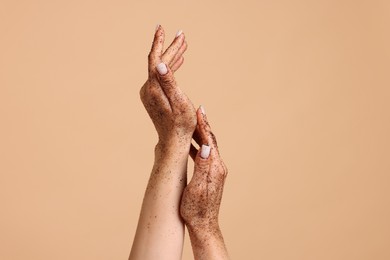 Photo of Woman applying body scrub onto her hands on beige background, closeup