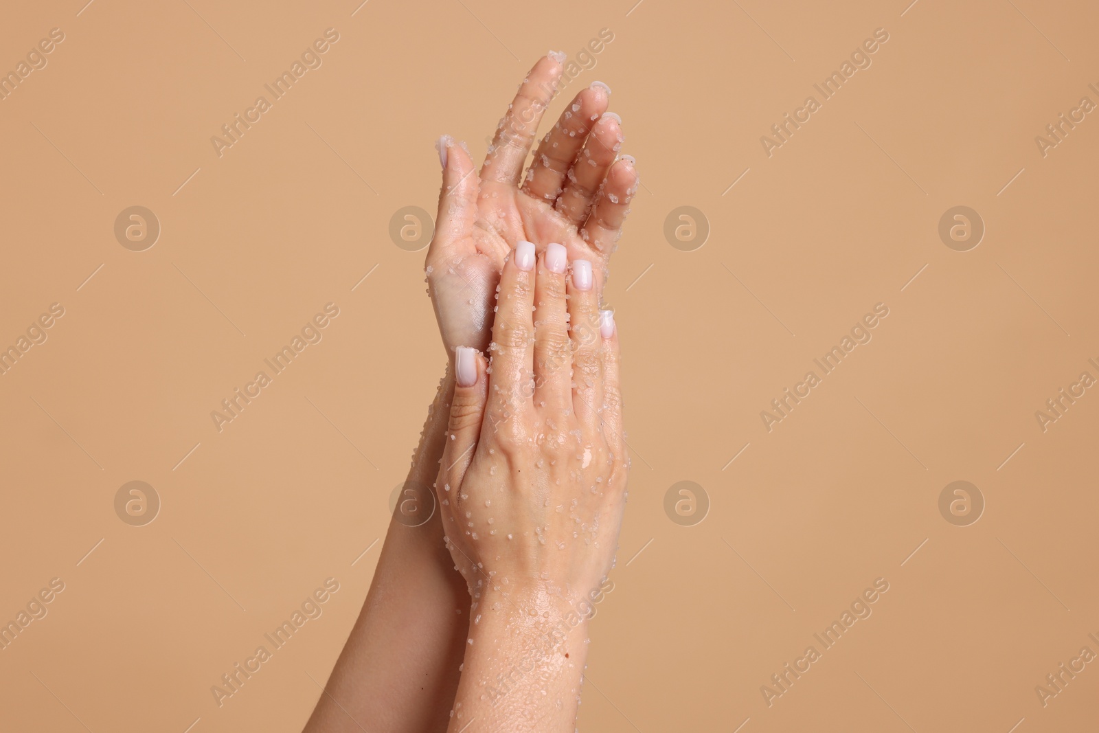 Woman applying body scrub onto her hands on beige background, closeup Photo of Woman applying body scrub onto her hands on beige background, closeup