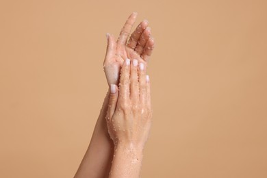 Photo of Woman applying body scrub onto her hands on beige background, closeup