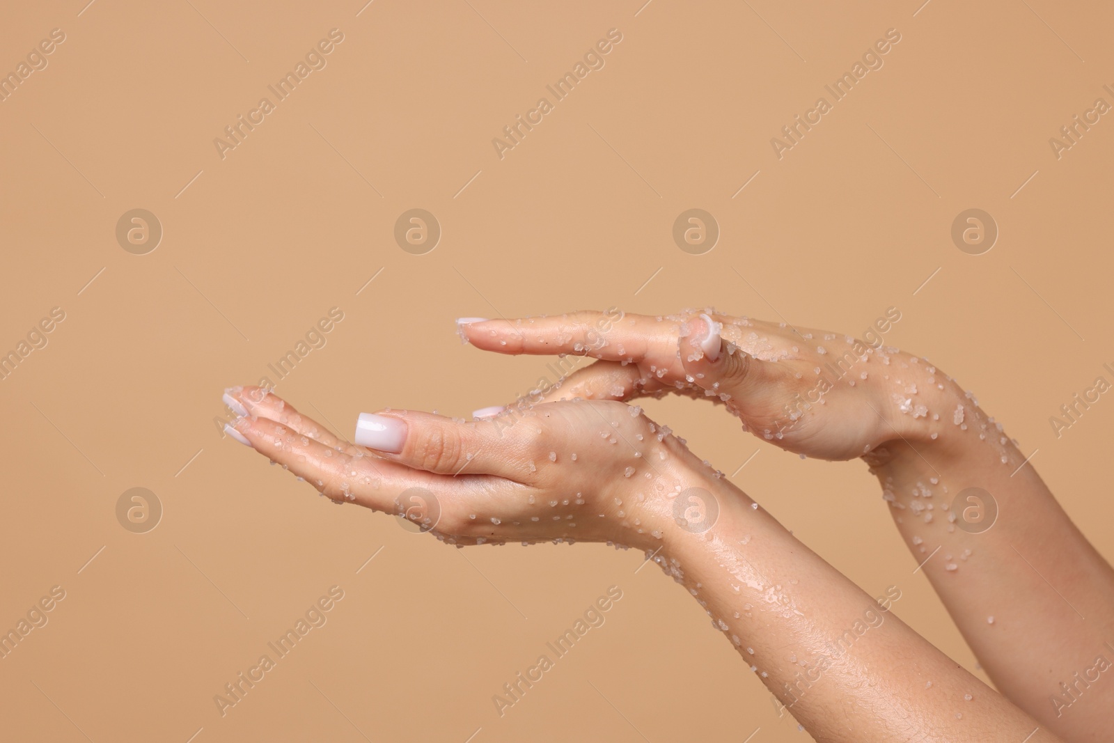 Woman applying body scrub onto her hands on beige background, closeup Photo of Woman applying body scrub onto her hands on beige background, closeup
