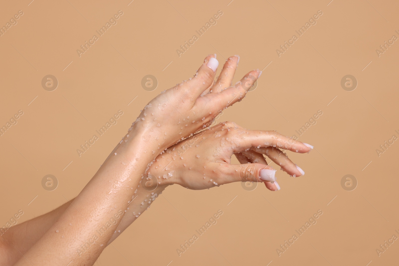 Woman applying body scrub onto her hands on beige background, closeup Photo of Woman applying body scrub onto her hands on beige background, closeup