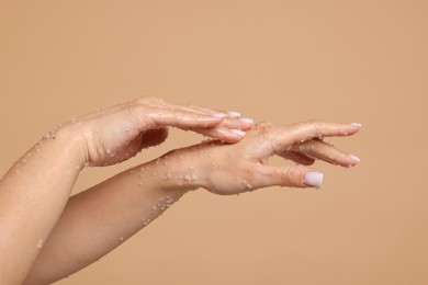 Photo of Woman applying body scrub onto her hands on beige background, closeup