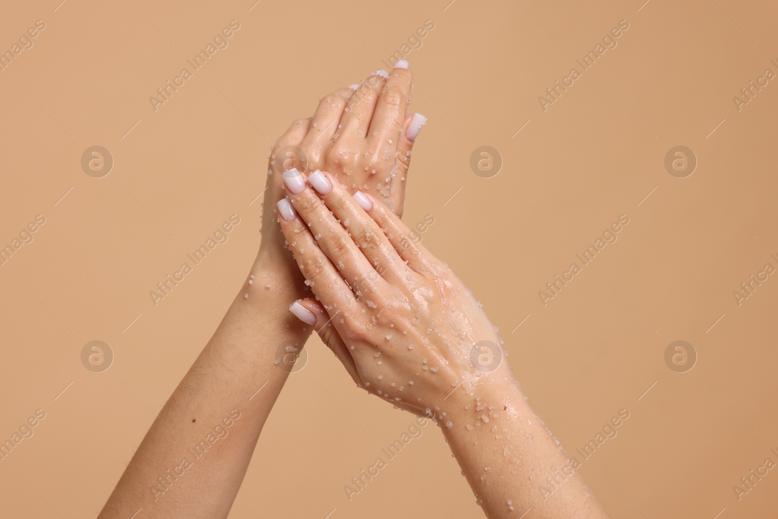 Woman applying body scrub onto her hands on beige background, closeup Photo of Woman applying body scrub onto her hands on beige background, closeup