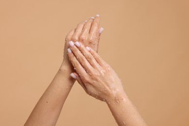Photo of Woman applying body scrub onto her hands on beige background, closeup