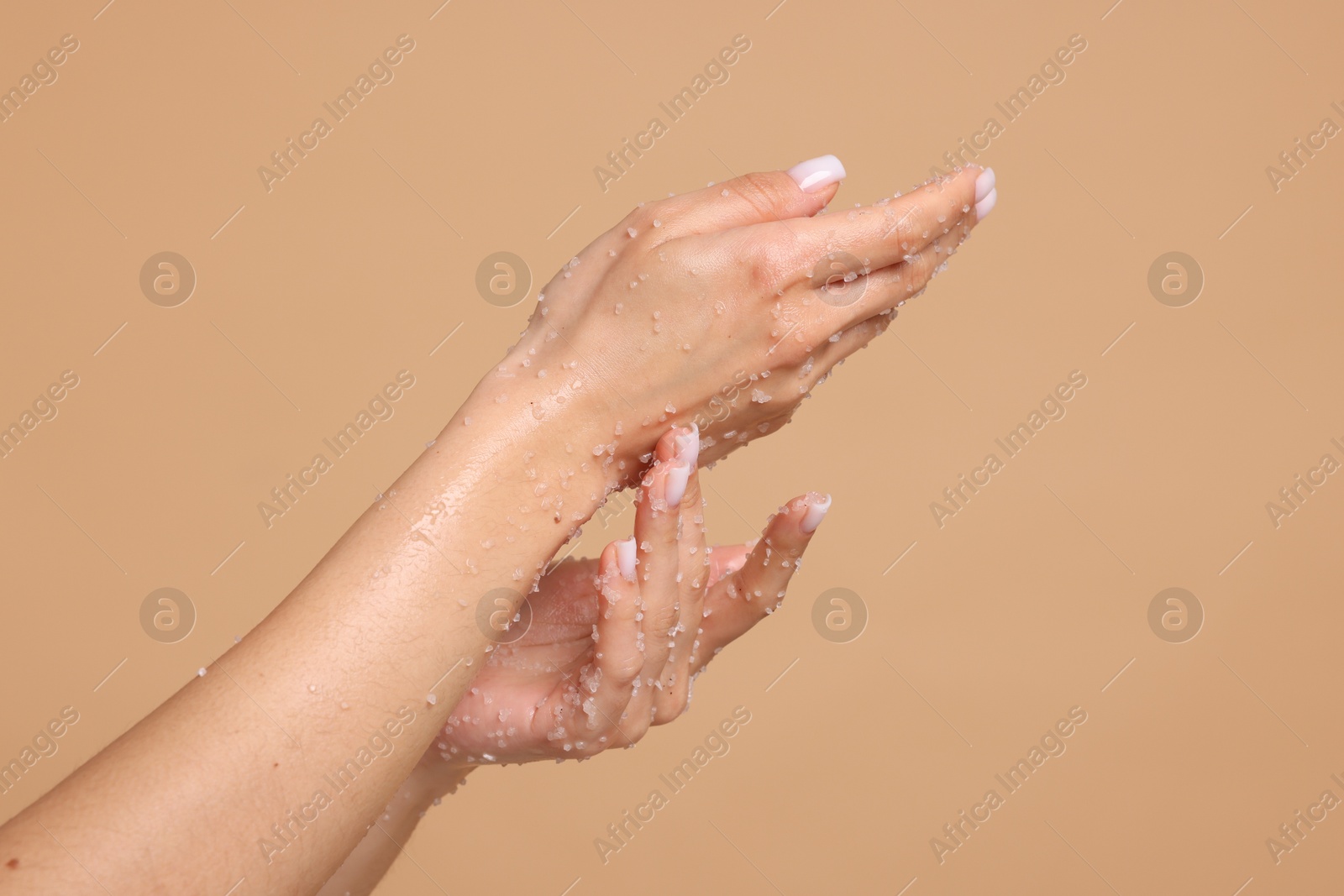 Woman applying body scrub onto her hands on beige background, closeup Photo of Woman applying body scrub onto her hands on beige background, closeup