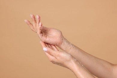 Photo of Woman applying body scrub onto her hands on beige background, closeup