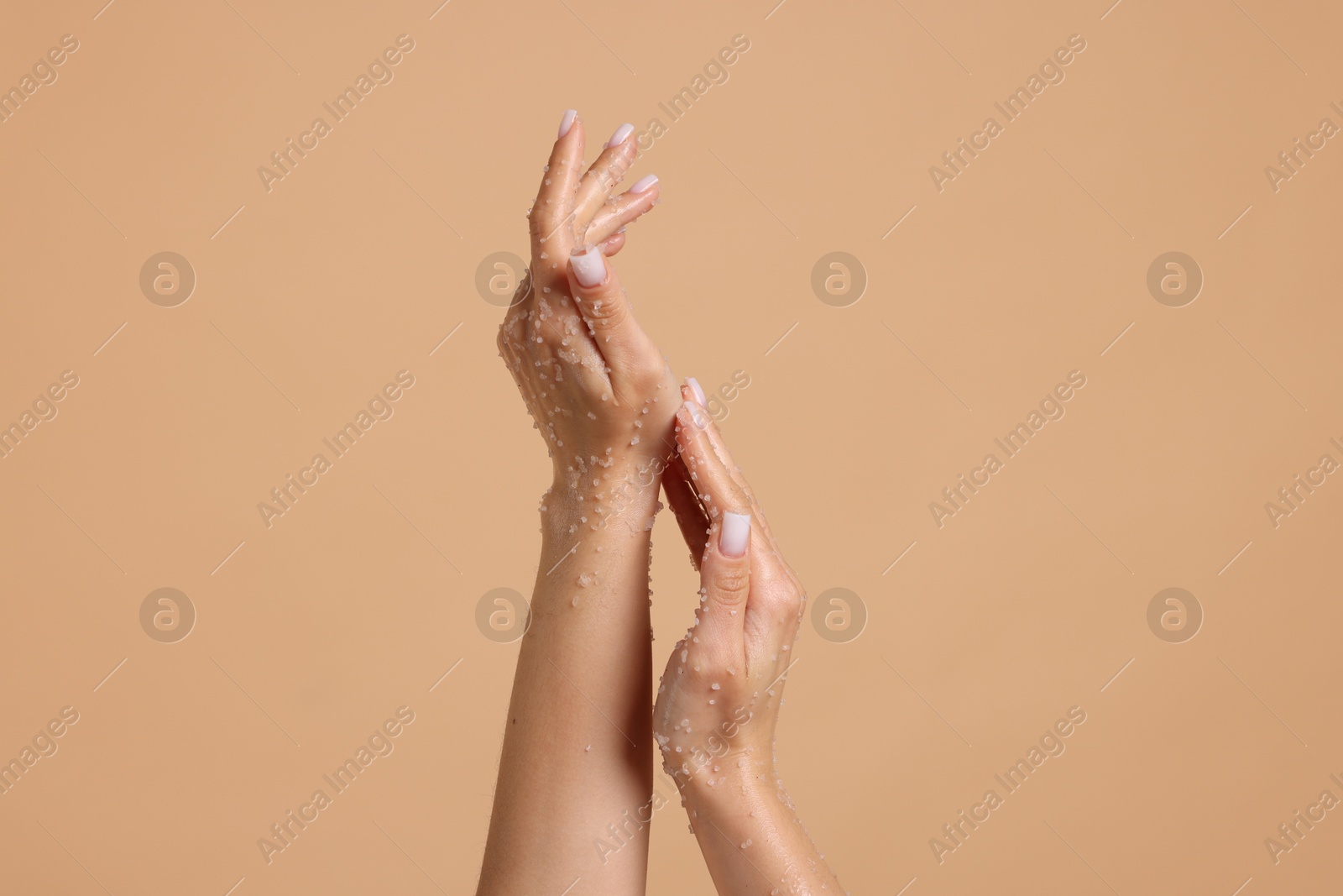 Woman applying body scrub onto her hands on beige background, closeup Photo of Woman applying body scrub onto her hands on beige background, closeup