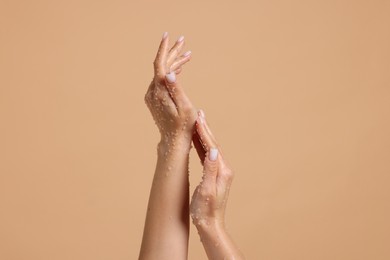 Photo of Woman applying body scrub onto her hands on beige background, closeup