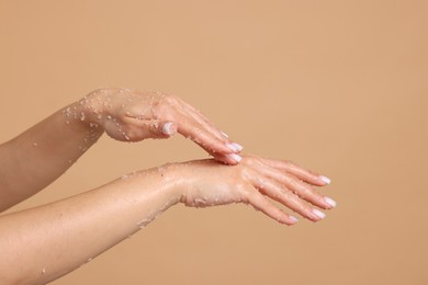 Photo of Woman applying body scrub onto her hands on beige background, closeup