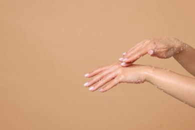 Photo of Woman applying body scrub onto her hands on beige background, closeup. Space for text