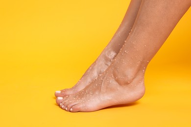 Photo of Woman with body scrub on her feet against orange background, closeup