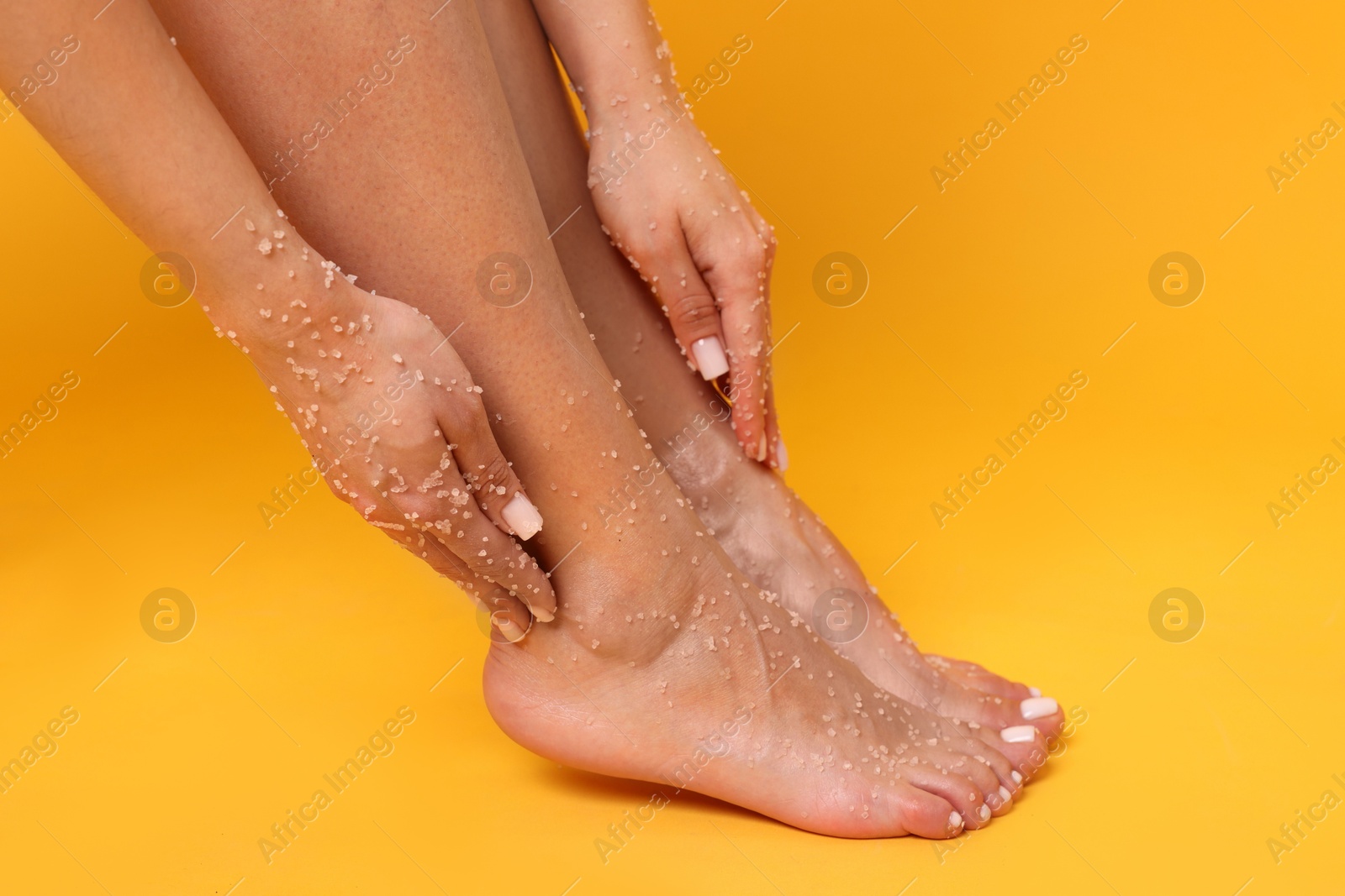 Woman applying body scrub onto her feet on orange background, closeup Photo of Woman applying body scrub onto her feet on orange background, closeup