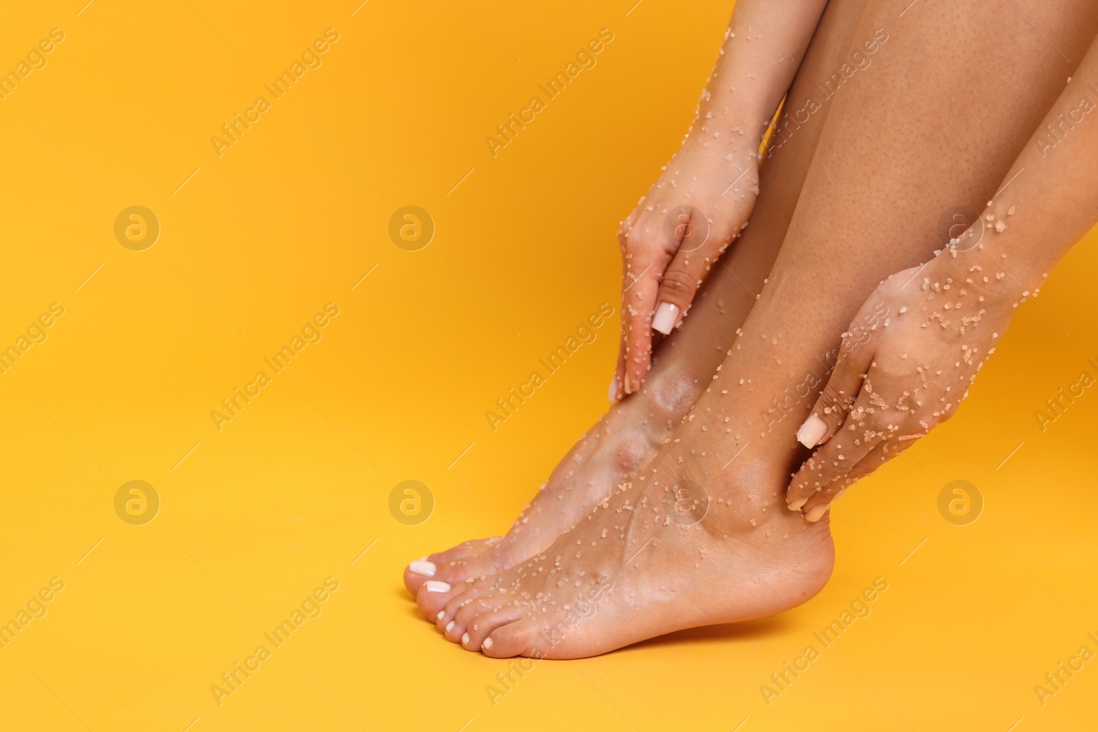 Woman applying body scrub onto her feet on orange background, closeup. Space for text Photo of Woman applying body scrub onto her feet on orange background, closeup. Space for text