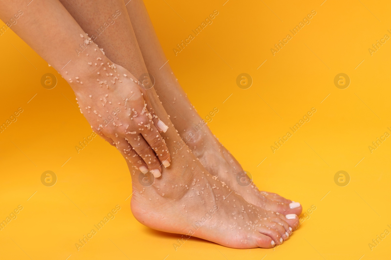 Woman applying body scrub onto her feet on orange background, closeup Photo of Woman applying body scrub onto her feet on orange background, closeup