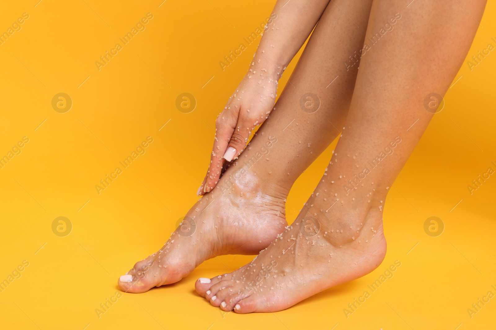 Woman applying body scrub onto her feet on orange background, closeup Photo of Woman applying body scrub onto her feet on orange background, closeup