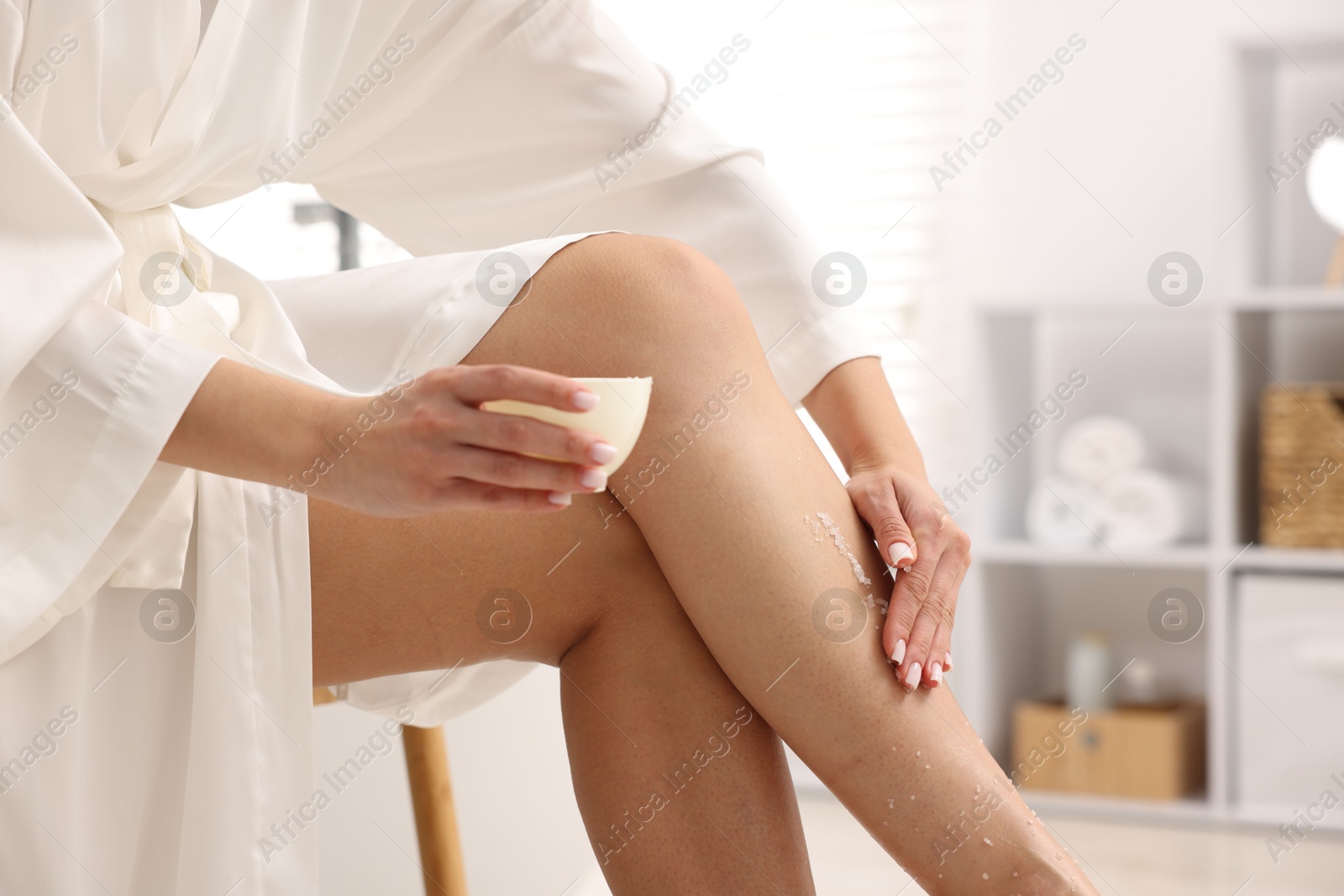 Woman applying body scrub onto her leg indoors, closeup Photo of Woman applying body scrub onto her leg indoors, closeup