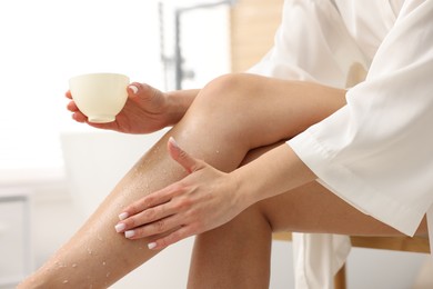 Photo of Woman applying body scrub onto her leg indoors, closeup