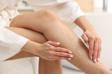 Photo of Woman applying body scrub onto her leg indoors, closeup
