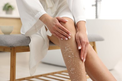 Photo of Woman applying body scrub onto her leg indoors, closeup
