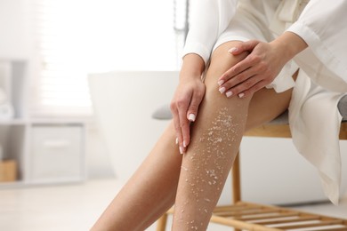 Photo of Woman applying body scrub onto her leg indoors, closeup. Space for text