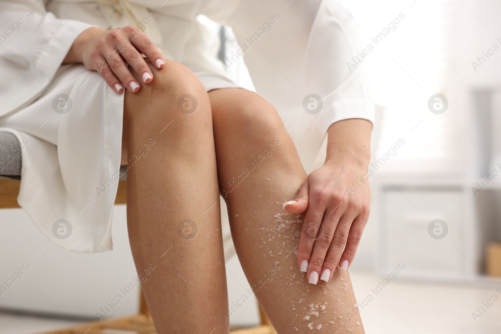 Woman applying body scrub onto her leg indoors, closeup Photo of Woman applying body scrub onto her leg indoors, closeup