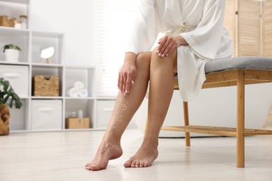 Photo of Woman applying body scrub onto her leg indoors, closeup. Space for text