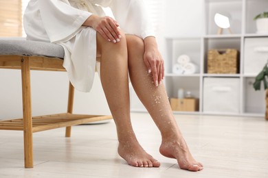 Photo of Woman applying body scrub onto her leg indoors, closeup. Space for text