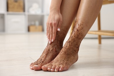 Photo of Woman applying body scrub onto her feet indoors, closeup