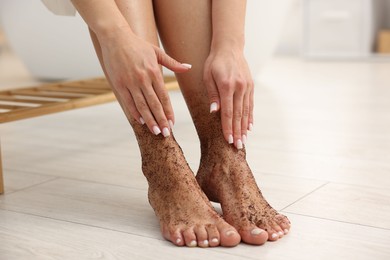 Photo of Woman applying body scrub onto her feet indoors, closeup