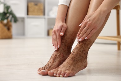 Photo of Woman applying body scrub onto her feet indoors, closeup. Space for text