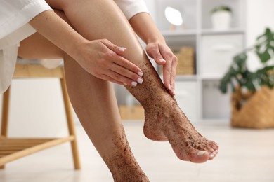 Photo of Woman applying body scrub onto her leg indoors, closeup