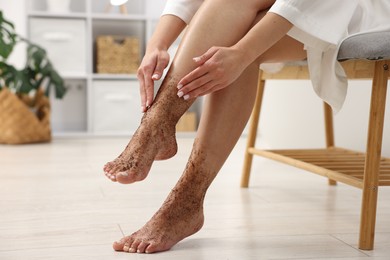 Photo of Woman applying body scrub onto her leg indoors, closeup