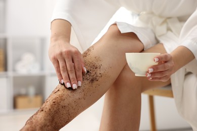 Photo of Woman applying body scrub onto her leg indoors, closeup