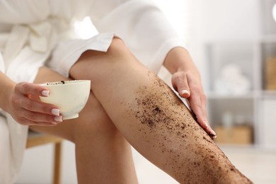Photo of Woman applying body scrub onto her leg indoors, closeup