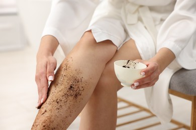 Photo of Woman applying body scrub onto her leg indoors, closeup